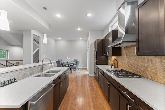 kitchen featuring stainless steel appliances, dark brown cabinetry, a sink, and wall chimney exhaust hood