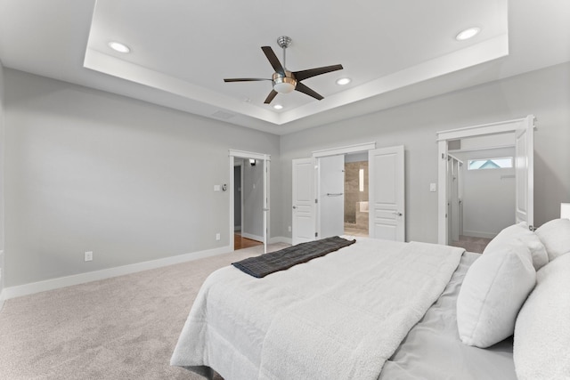 bedroom with recessed lighting, connected bathroom, baseboards, and a tray ceiling