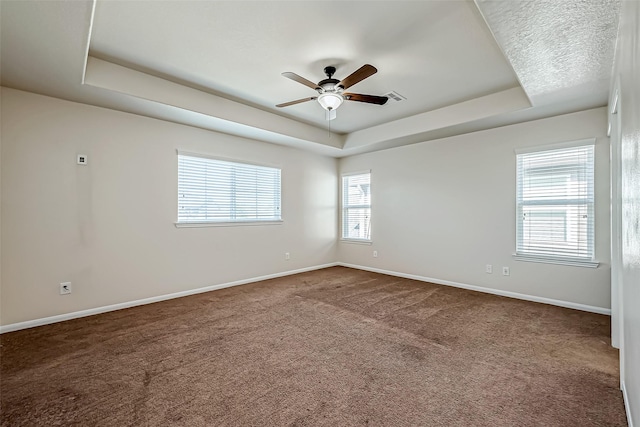 empty room featuring visible vents, dark carpet, baseboards, ceiling fan, and a tray ceiling