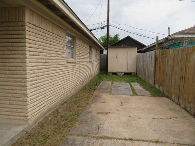 view of side of home with an outbuilding, a patio area, brick siding, a fenced backyard, and a storage unit