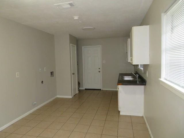 kitchen featuring dark countertops, a sink, white cabinetry, baseboards, and light tile patterned floors