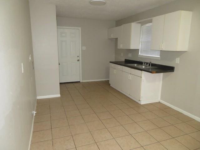 kitchen featuring a sink, dark countertops, white cabinets, and baseboards