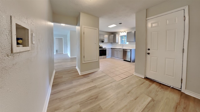 kitchen featuring appliances with stainless steel finishes, gray cabinetry, light countertops, light wood-type flooring, and a textured wall