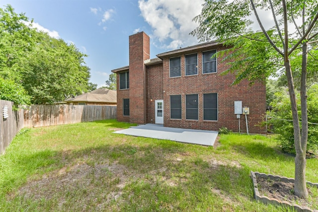 back of property with a patio, a fenced backyard, a chimney, brick siding, and a lawn