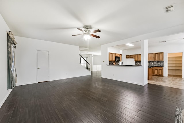 unfurnished living room with ceiling fan, baseboards, wood finished floors, visible vents, and stairway