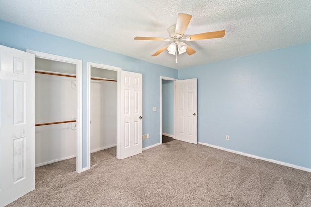 unfurnished bedroom with baseboards, carpet, two closets, and a textured ceiling