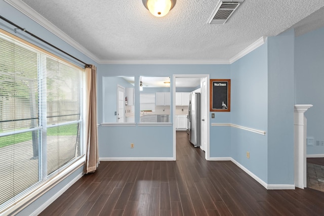 empty room with a textured ceiling, visible vents, crown molding, baseboards, and dark wood-type flooring