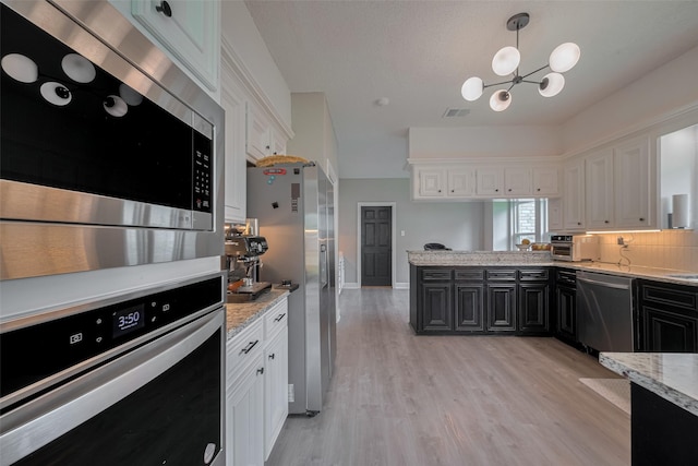 1709 Coles Farm Dr, Sugar Land, TX 77478 - kitchen featuring appliances with stainless steel finishes, dark cabinetry, white cabinets, a chandelier, and light wood-style floors