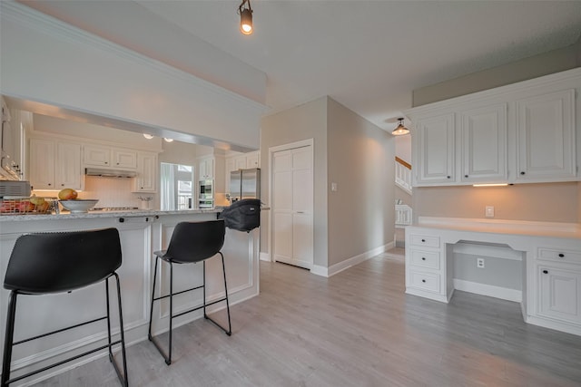 1709 Coles Farm Dr, Sugar Land, TX 77478 - kitchen with white cabinetry, a breakfast bar, a peninsula, under cabinet range hood, and light wood finished floors