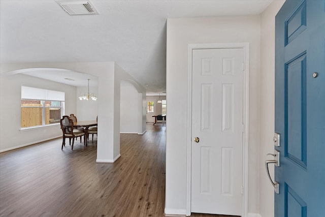 foyer entrance featuring arched walkways, dark wood-type flooring, a chandelier, and baseboards