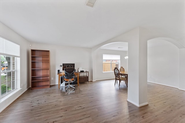 office space with arched walkways, wood finished floors, and baseboards
