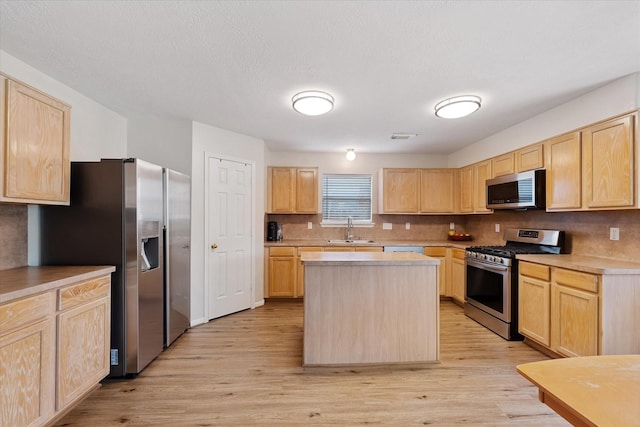 kitchen with appliances with stainless steel finishes, light brown cabinets, a sink, and light wood-type flooring