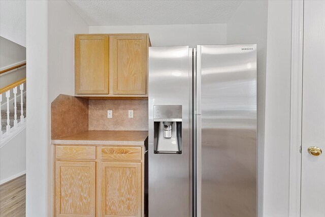 kitchen with stainless steel refrigerator with ice dispenser, light brown cabinetry, light countertops, and backsplash