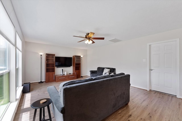 living area with wood finished floors, a ceiling fan, and baseboards