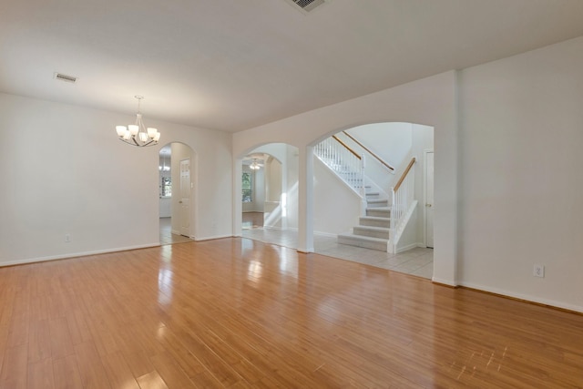2712 Park Falls Dr, Pearland, TX 77584 - unfurnished living room featuring arched walkways, stairs, light wood finished floors, a chandelier, and baseboards