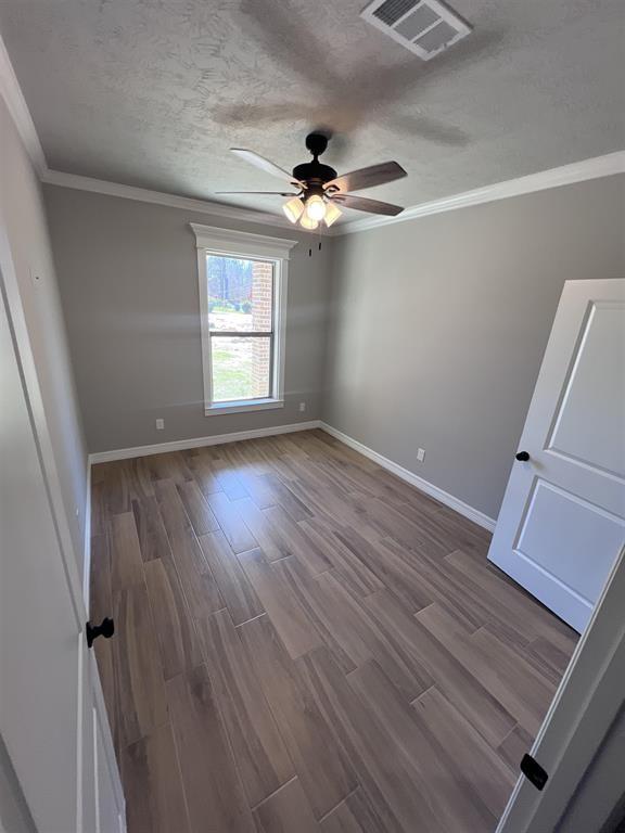7510 Tram Rd, Beaumont, TX 77713 - spare room featuring a ceiling fan, baseboards, wood finished floors, visible vents, and ornamental molding
