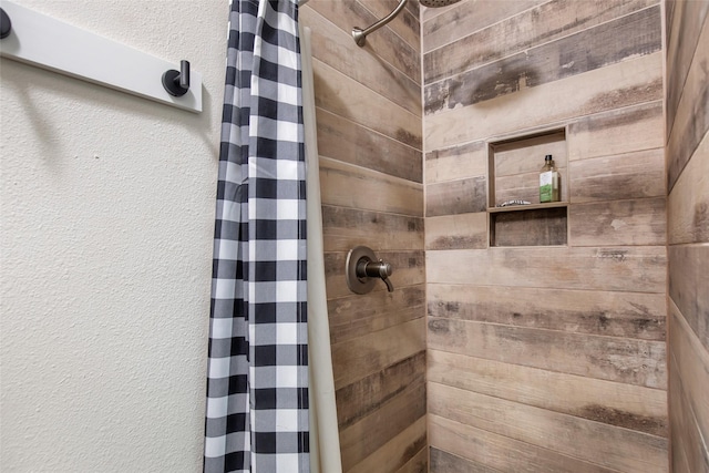 bathroom with a textured wall and a tile shower