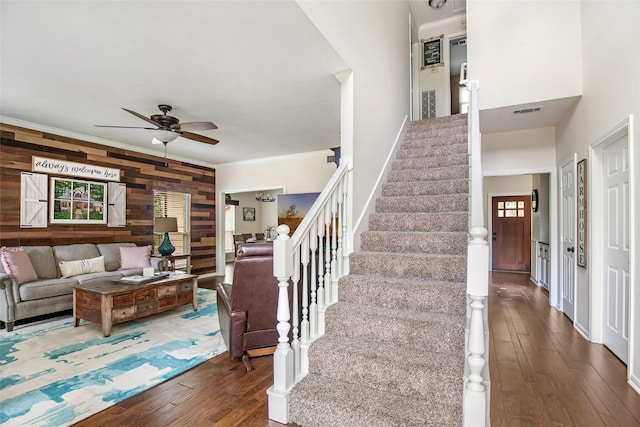 stairway with wood-type flooring, a ceiling fan, wood walls, and visible vents