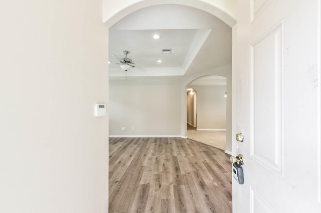interior space featuring light wood-style floors, arched walkways, a ceiling fan, recessed lighting, and a tray ceiling
