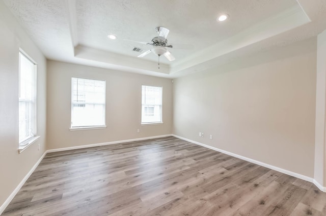 empty room featuring light wood-style floors, a raised ceiling, recessed lighting, and visible vents