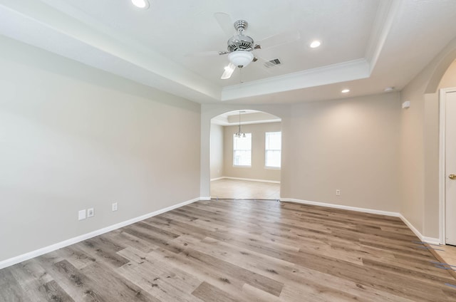 unfurnished room featuring arched walkways, ceiling fan, baseboards, and a tray ceiling
