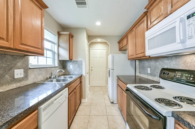 kitchen with visible vents, arched walkways, dark countertops, a sink, and white appliances