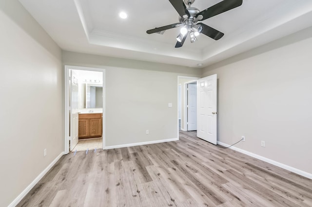 unfurnished bedroom featuring baseboards, light wood-style flooring, and a raised ceiling