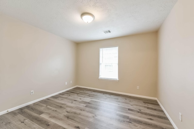 unfurnished room with visible vents, a textured ceiling, baseboards, and wood finished floors