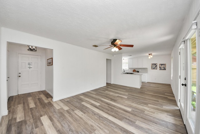 unfurnished living room with a textured ceiling, ceiling fan with notable chandelier, and wood finished floors