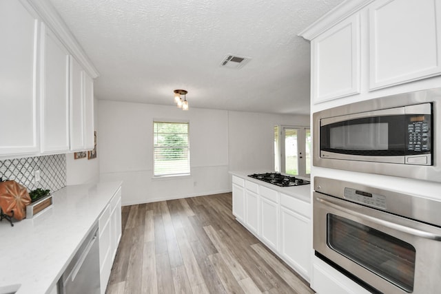 kitchen with visible vents, light wood-style floors, white cabinets, backsplash, and stainless steel appliances