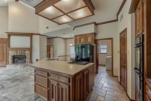 kitchen with stone tile flooring, black appliances, a sink, ornamental molding, and a fireplace