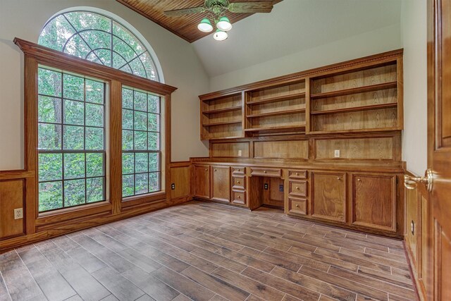 unfurnished office featuring ceiling fan, a wainscoted wall, built in desk, high vaulted ceiling, and wood finished floors