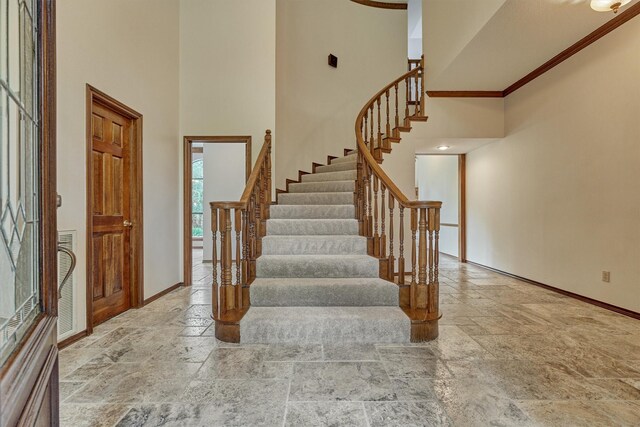 entrance foyer featuring stone tile floors, baseboards, a towering ceiling, stairway, and crown molding