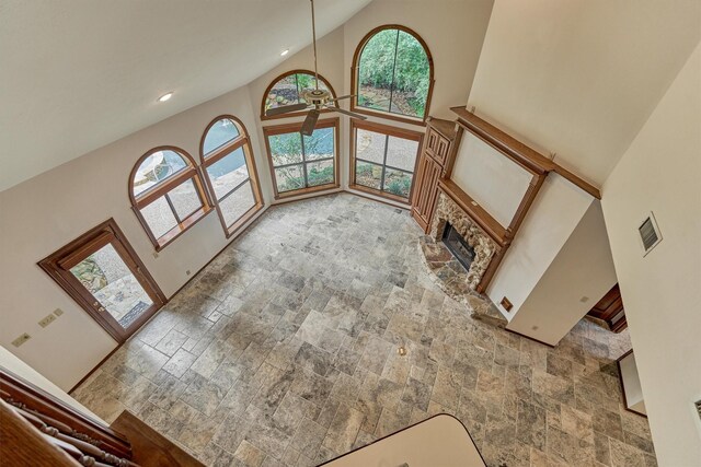 unfurnished living room featuring high vaulted ceiling, stone tile flooring, a ceiling fan, a stone fireplace, and recessed lighting