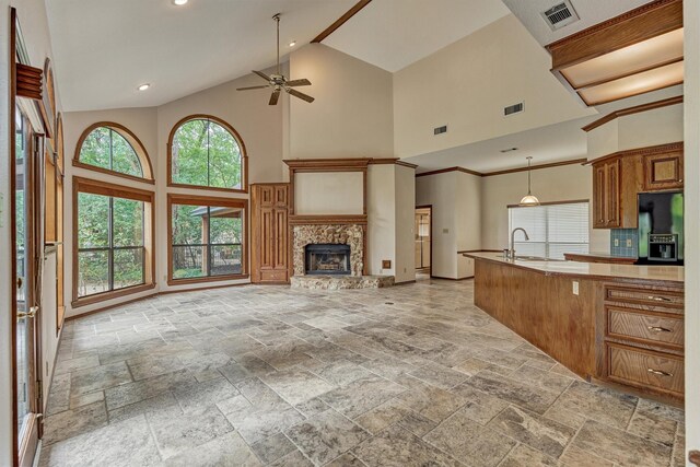 kitchen featuring high vaulted ceiling, a ceiling fan, open floor plan, stone tile floors, and a fireplace