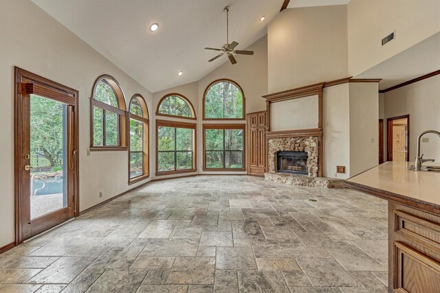 unfurnished living room with stone tile floors, high vaulted ceiling, a ceiling fan, a sink, and plenty of natural light