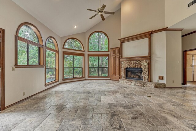 unfurnished living room featuring high vaulted ceiling, ceiling fan, healthy amount of natural light, stone tile flooring, and a stone fireplace