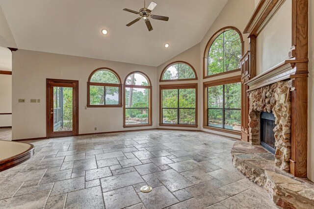 unfurnished living room with baseboards, stone tile flooring, ceiling fan, healthy amount of natural light, and high vaulted ceiling