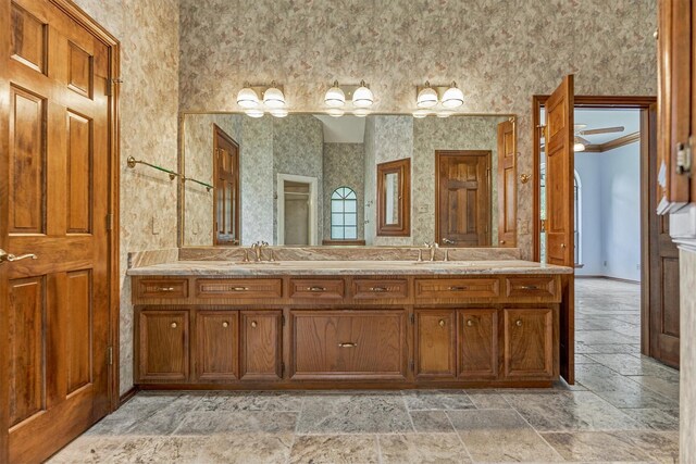 full bathroom featuring stone tile floors, double vanity, and wallpapered walls