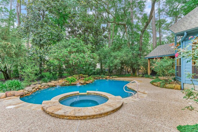 view of pool with a pool with connected hot tub, a patio area, fence, and view of wooded area