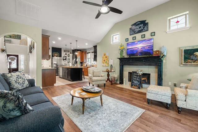 living area featuring ceiling fan, visible vents, a tile fireplace, high vaulted ceiling, and light wood-style floors