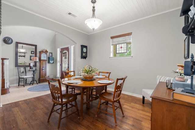 dining space with crown molding, arched walkways, baseboards, wood finished floors, and visible vents