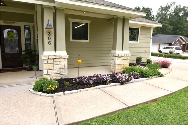 view of exterior entry featuring covered porch, a shingled roof, and stone siding