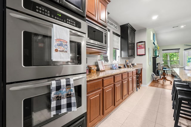 kitchen with light stone counters, appliances with stainless steel finishes, light tile patterned flooring, and brown cabinets