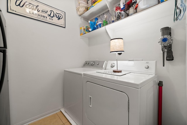 washroom featuring laundry area, baseboards, light tile patterned flooring, and washer and dryer
