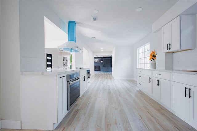 1719 Wagon Gap Trl, Houston, TX 77090 - kitchen featuring stainless steel oven, island exhaust hood, white cabinetry, light wood-style floors, and baseboards