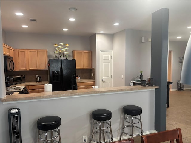 16427 Kettlebrook Ln, Houston, TX 77049 - kitchen featuring backsplash, a kitchen bar, visible vents, light brown cabinetry, and black appliances