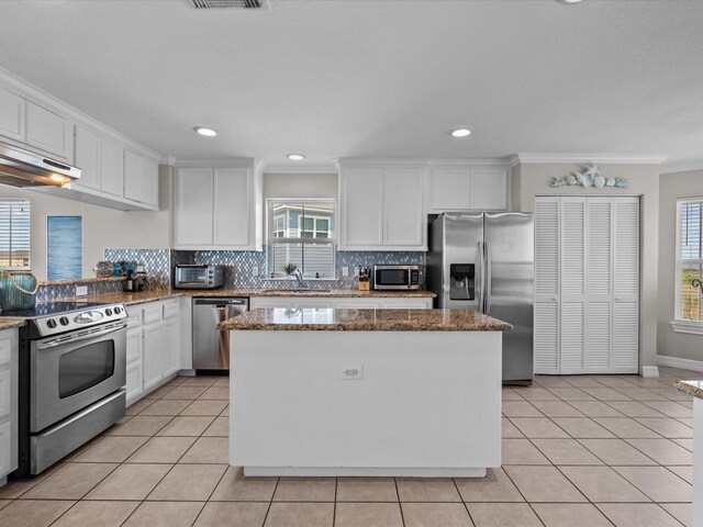 4035 Estuary Ct, Galveston, TX 77554 - kitchen featuring appliances with stainless steel finishes, white cabinetry, a kitchen island, tasteful backsplash, and light tile patterned floors