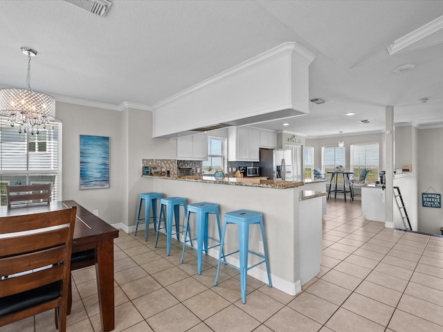 4035 Estuary Ct, Galveston, TX 77554 - kitchen featuring light tile patterned floors, stainless steel fridge, a peninsula, white cabinetry, and a chandelier