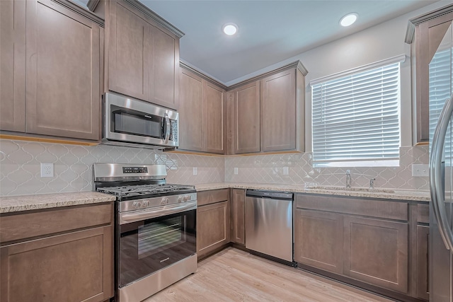 kitchen featuring stainless steel appliances, light stone counters, a sink, and light wood finished floors